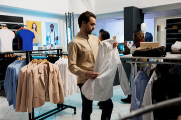 Man holding shirt on hanger, examining style and purchasing casual wear in fashion retail store....