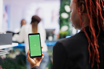 African american woman using smartphone with green screen while shopping for clothes in mall....