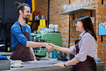 Young man in apron shaking hands with woman owner of coffee shop