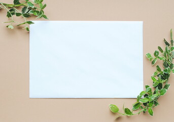 Frame of green leaves of small branches around a white leaf on a beige background. Place for text, postcard, top view, copy.
