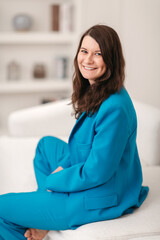 Beautiful happy woman smiling. She is sitting in the interior in a blue business suit. Vertical frame.