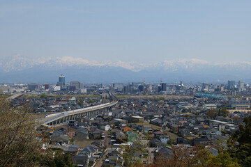 満開の桜春霞の薬師岳北アルプス立山連峰と富山市街地と北陸新幹線、神通大橋