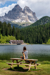 Woman sitting on a table admiring the views of a lake surrounded by mountains and pine trees. Misurina Lake. Dolomites. Italy