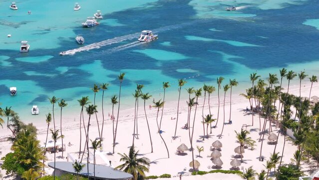 Aerial flight above palm trees on the public Bavaro beach with white sand. Turquoise water of the Caribbean sea and excursion yachts and boats. Punta Cana, Dominican republic