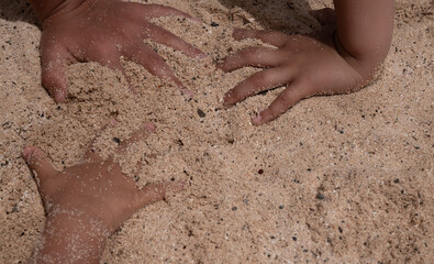 Two hands are in the sand, one of which is slightly higher than the other. The sand is a light brown color and the hands are covered in it © Jonathan