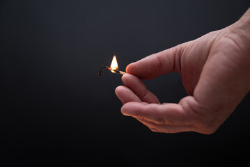 A hand holding a matchstick with a small flame. Concept of warmth and comfort, as the flame is a...
