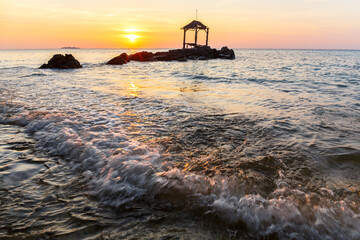 Sunset at a beach in Indonesia with rocks and a little hut in the water