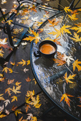 Cup of coffee standing on the patio table after the fall rain with lots of fallen maple leaves