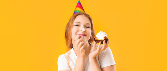Beautiful young happy woman with birthday cupcake on yellow background