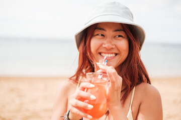 Woman of Asian origin having a cocktail on a day at the beach. Concept: summer, heat, enjoy