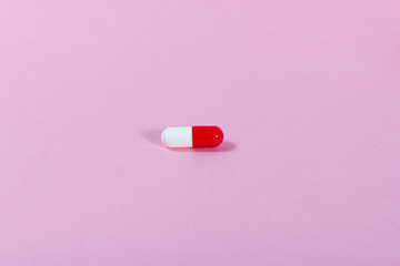 Close-up of a red and white medicinal tablet on a pink background.