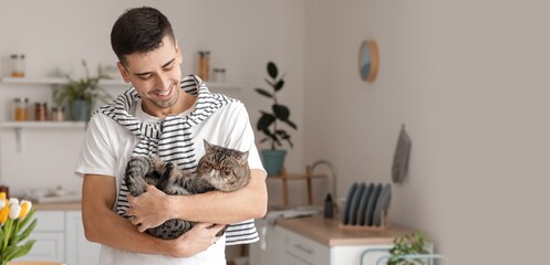 Young man with cute cat in kitchen