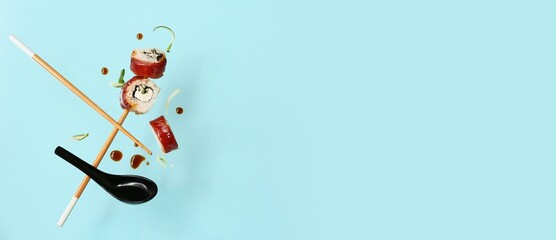 Tasty flying sushi rolls, chopsticks and soy sauce on light blue background with space for text