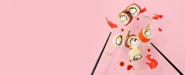 Tasty flying sushi rolls, chopsticks, soy sauce and ginger on pink background with space for text