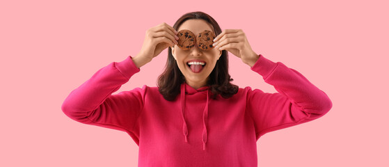 Funny young woman with tasty cookies on pink background