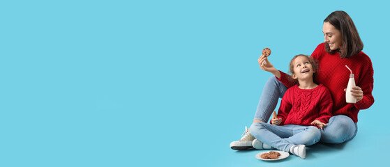 Young mother and her little daughter drinking milk with cookies on blue background