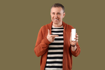 Mature man pointing at mobile phone on green background