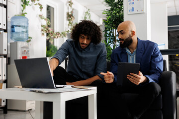 Entrepreneur and colleague discussing project while analyzing data on laptop in business office....