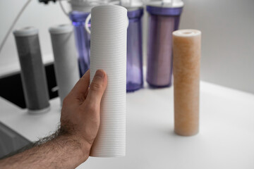 Man hand holding clean filter for reverse osmosis for water purification on the table in the kitchen. Clean and dirty filters after replacement. 