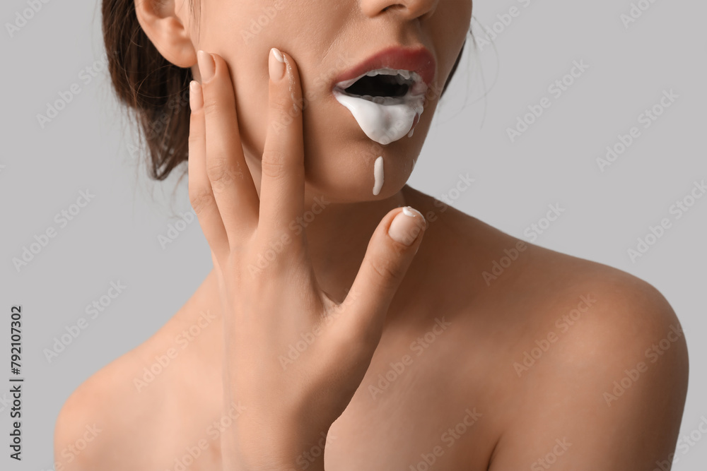 Poster Young woman with white liquid in her mouth on light background, closeup. Sex concept