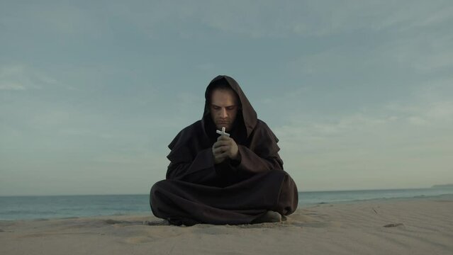 Monk Collected In Prayer Sitting On The Beach In The Evening