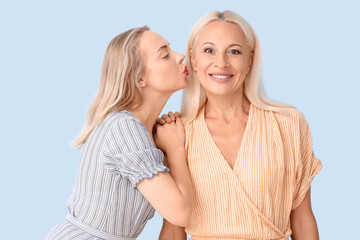 Happy young beautiful woman kissing her mother on blue background