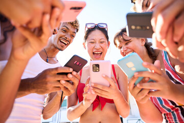 Low angle view of a group of diverse friends gathered in a beach in circle with their mobile...