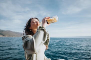 A happy girl enjoys a refreshing drink by the ocean, embodying joy and relaxation under a clear...