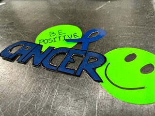 A sticker with a smiling face and the word "cancer" written in blue and green
