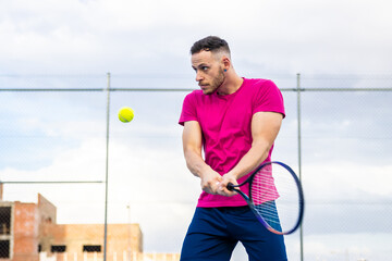 A man in a pink shirt is playing tennis with a yellow ball