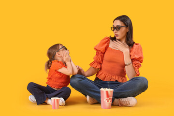Beautiful mother and her cute little daughter in 3D glasses with buckets of popcorn on yellow...