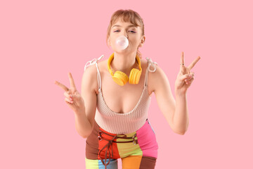 Beautiful young woman with chewing gum showing victory gesture on pink background