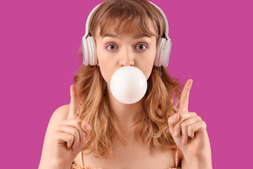 Young woman in headphones with chewing gum pointing at something on purple background, closeup