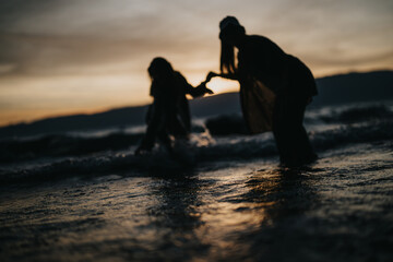 Silhouettes of two girls happily playing in the lake waters at sunset, embodying joy and...
