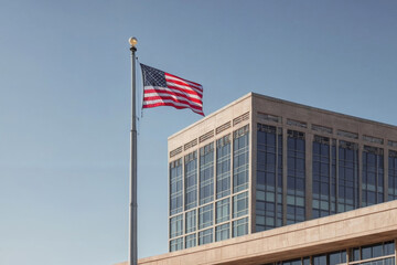 The image shows a modern architectural building with a large American flag waving in the wind in front of it. The building has a lot of glass windows and a grey concrete exterior