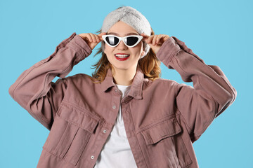 Smiling young woman in headband with sunglasses on blue background