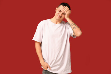 Handsome ashamed young man covering face with hand on red background