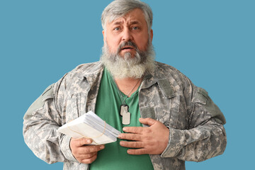 Portrait of sad senior man in military uniform holding letters on blue background - obrazy, fototapety, plakaty
