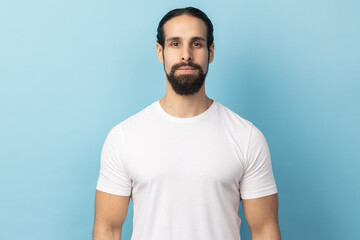Portrait of bearded handsome man wearing white T-shirt standing looking at camera with serious...