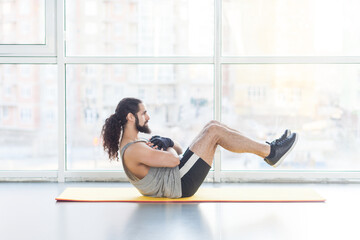 Side view portrait of powerful man with curly long hair having workout in gym doing crunches,...