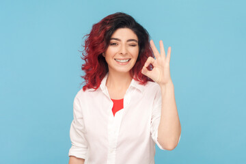 Portrait of cheerful adult woman with fancy red hair showing okay sign, assures you everything is...