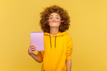 Portrait of funny silly woman with Afro hairstyle holding organizer with empty paper and pencil...