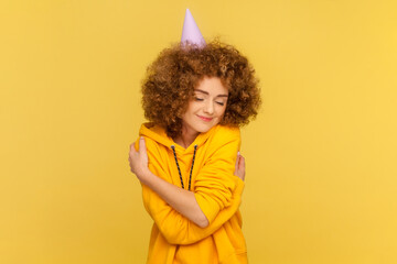 Portrait of egoistic satisfied woman in party cone with Afro hairstyle celebrating her birthday,...