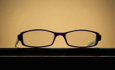  Reading glasses on the table, purple glasses frames on a yellow/beige background, close-up,...