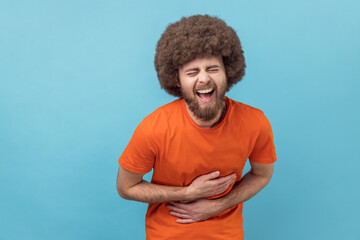 Portrait of laughing man with Afro hairstyle in orange T-shirt holding his stomach and hunched in...