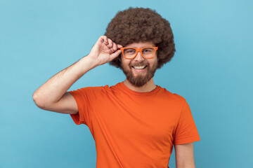 Portrait of smiling optimistic man with Afro hairstyle wearing orange T-shirt buying new...