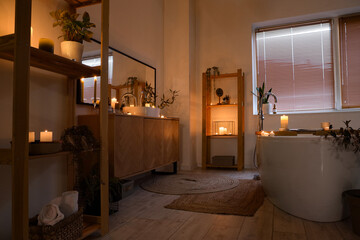 Interior of bathroom with burning candles, sink and bathtub in evening