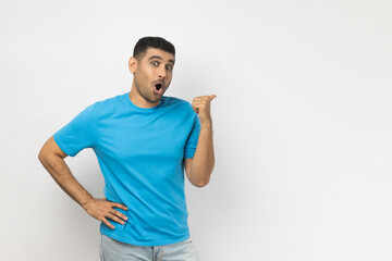 Portrait of amazed shocked young adult unshaven man wearing blue T- shirt standing indicating at...