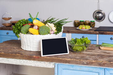 Tablet with blank screen copy space for advertisement of healthy vegetarian low-calorie diet, food recipes, menu and blog, fresh vegetables on wooden table in modern kitchen.