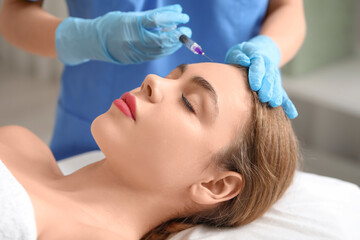 Pretty young woman receiving filler injection in beauty salon